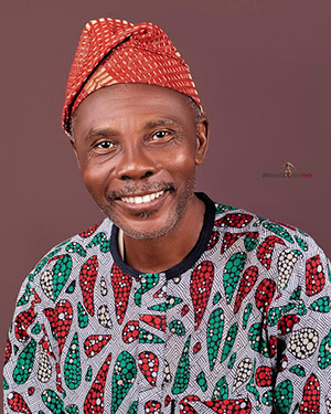 A smiling man wearing a red, green and white print shirt and an orange and yello hat.